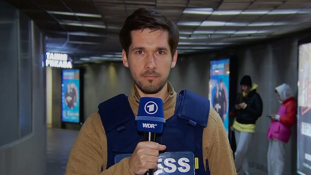 ARD Reporter Vassili Golod während einer Liveschalte mit Schutzweste an und Mikrofon in der Hand 