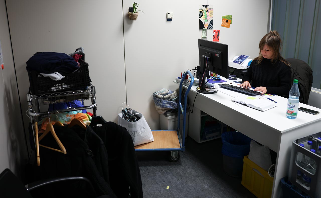 Büro von Streetworkerin Kristina Wessel. Sie sitze am Schreibtisch. Vor ihr ist ein kleiner Kleiderständer mit Kleidung darauf.
