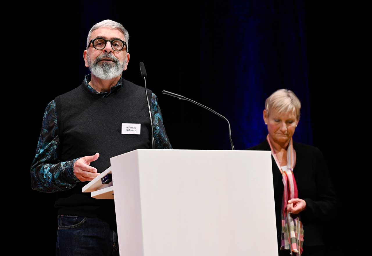 Matthias Schwarz spricht vorm Mikrofon über Missbrauch in der evangelischen Kirche. Im Hintergrund die Ratsvorsitzende Kirsten Fehrs.