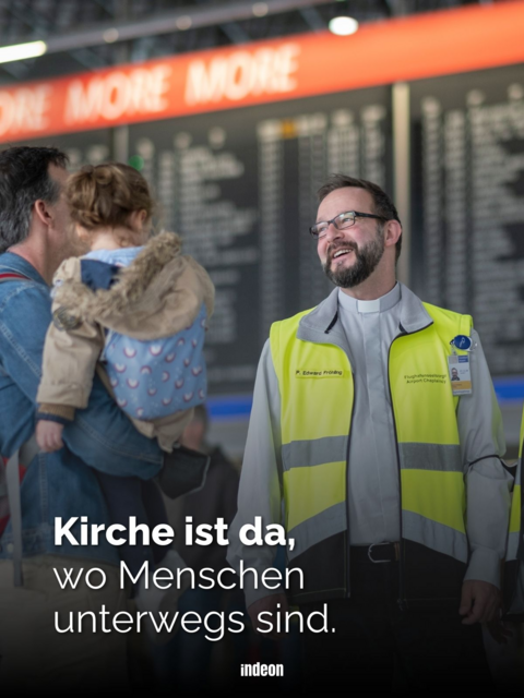 lachender Mann mit Warnweste vor Flughafentafel schaut Vater mit Kind auf Arm an