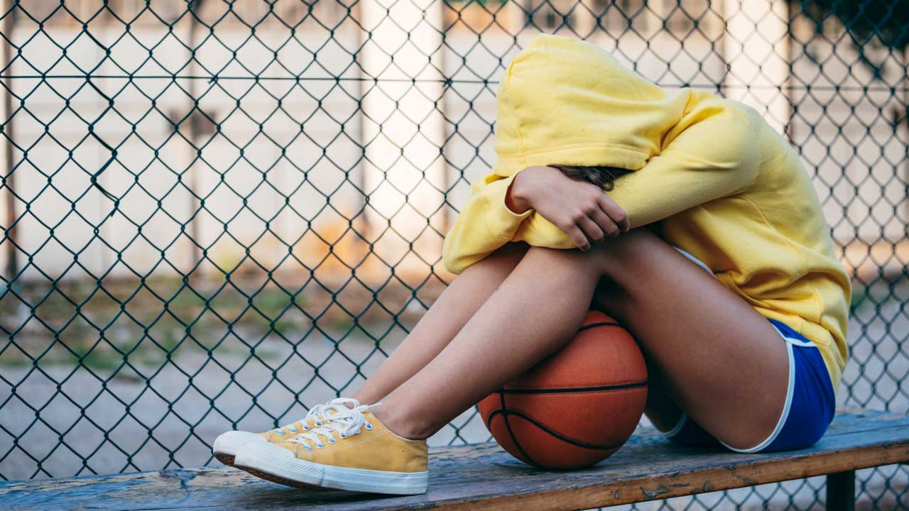 Mädchen kümmert sich zusammen, zwischen ihren Beinen ein Basketball