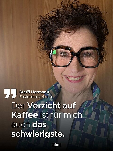 Eine Frau mit kurzen dunklen Locken und schwarzer markanter Brille steht vor einer holzvertäfelten Wand. Sie lächelt. Text: Fastenkursleiterin Steffi Hermann „Der Verzicht auf Kaffee ist für mich auch das schwierigste".