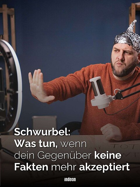 Ein Mann mit einem Hut aus Alufolie sitzt vor einem Podcast-Mikrophon. Er blickt kritisch und hebt abwehrend die rechte Hand. Text: Schwurbel: was tun, wenn dein Gegenüber keine Fakten mehr akzeptiert.