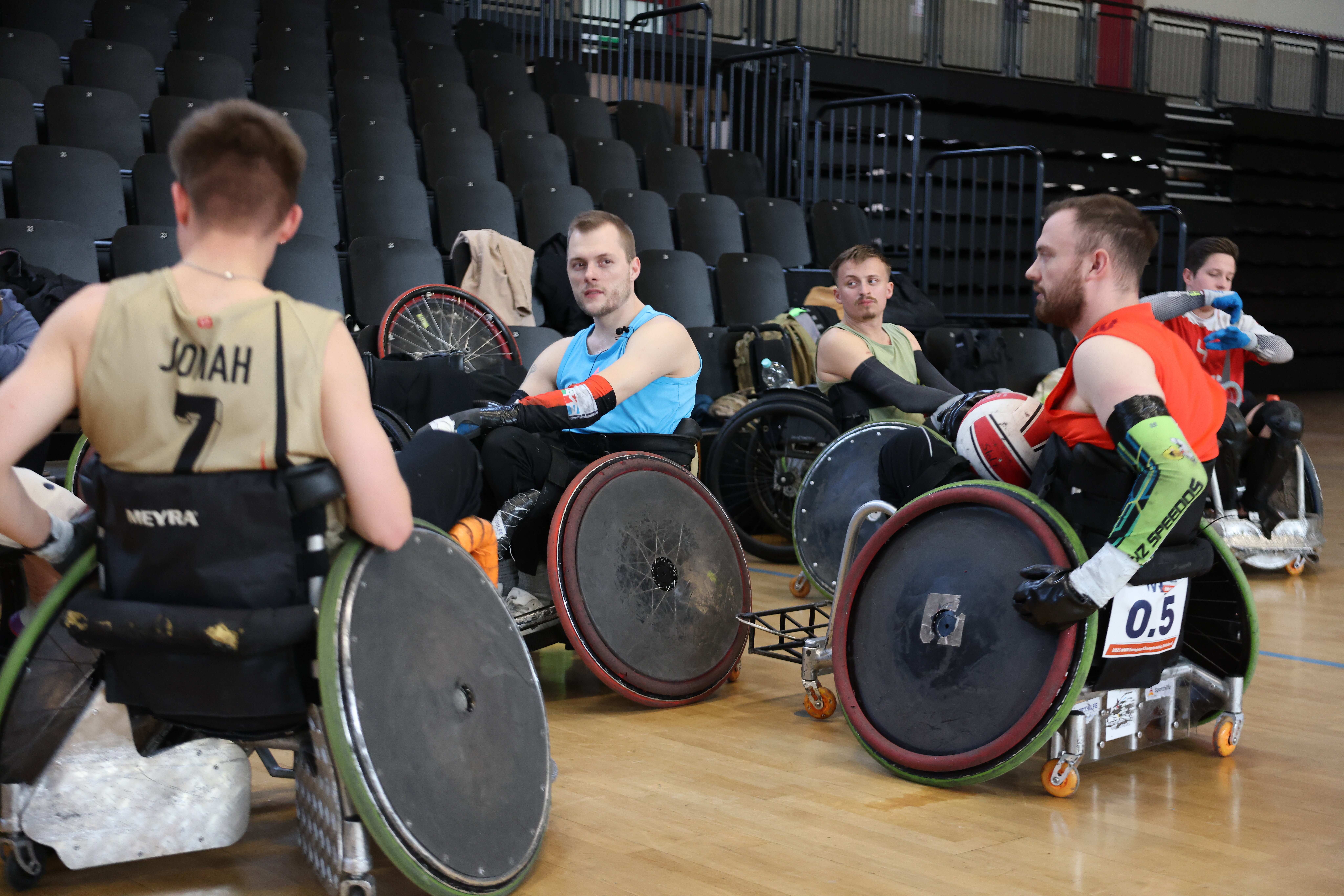 Florian sitzt in einem Sportrollstuhl umringt von seinen Teamkollegen und schaut fokussiert aufs Spielfeld. 