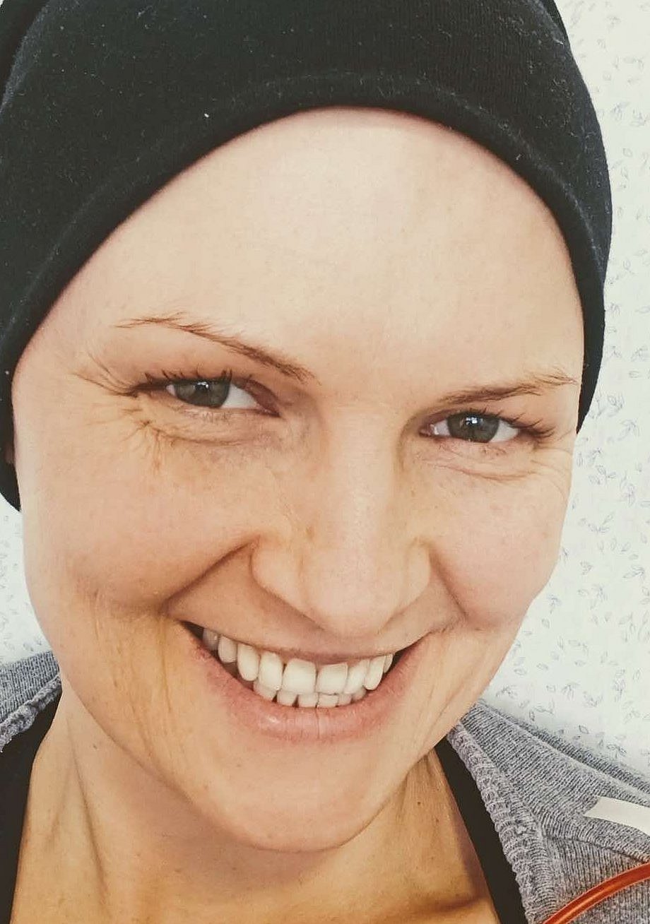 Das Porträtfoto von Olga zeigt die junge Frau lachend und mit einem schwarzen Kopftuch. An ihrer rechten Schulter hängt ein roter Schlauch.