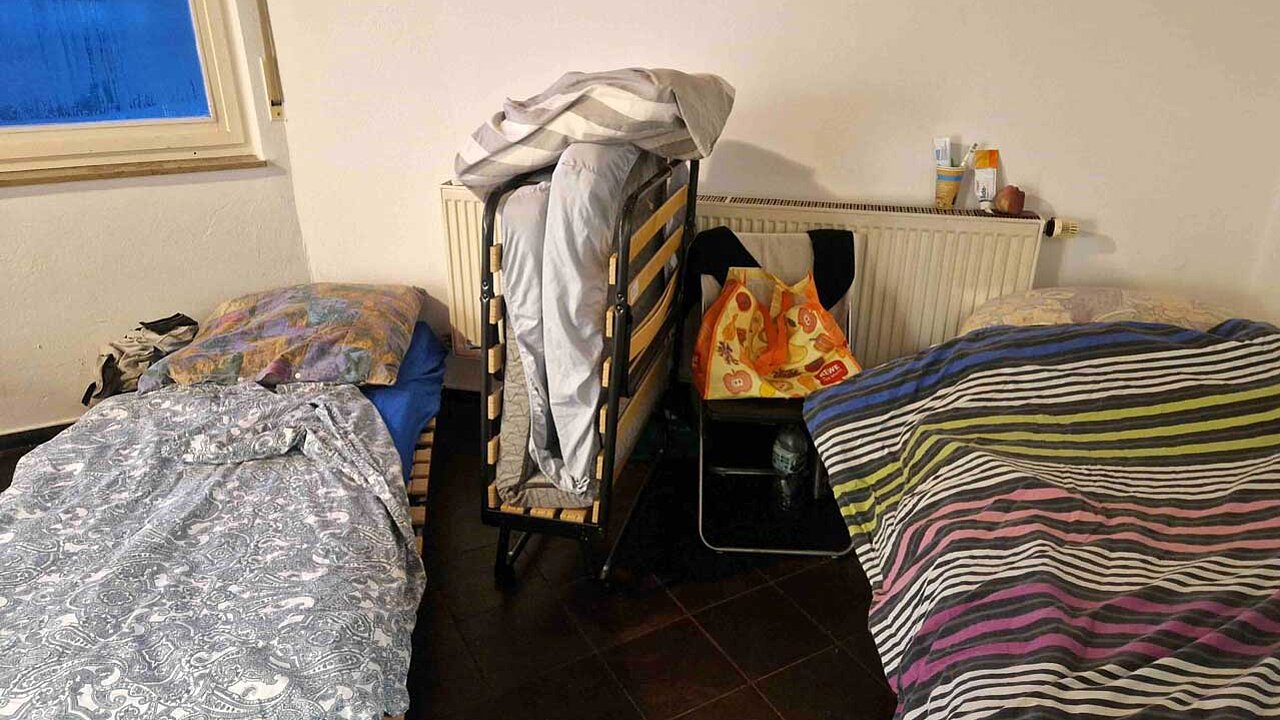 2 aufgeklappte Klappbetten in einem Raum. Dazwischen steht noch ein zusammengeklapptes Bett.