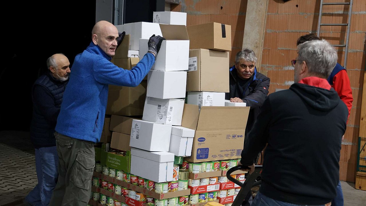 4 Ehrenamtliche fahren eine vollgepackte Europalette mit einem Hubwagen durch eine Lagerhalle