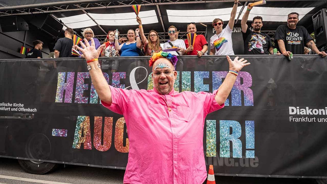 Nulf Schade-James, Pfarrer seit 1989 in der Kirchengemeinde Frieden und Versöhnung in Frankfurt, steht zu Beginn der Christopher Street Day Parade (CSD) in Frankfurt vor dem LKW der evangelischen Kirche. Das Motto des CSD, „Here and queer - auch wir“, steht auf den großen Schildern an den Längsseiten des Lkw, auf dem Pfarrpersonen, Gemeindemitglieder und Kolleg*innen anderer Berufe mitfahren (Foto vom 15.07.2023).
