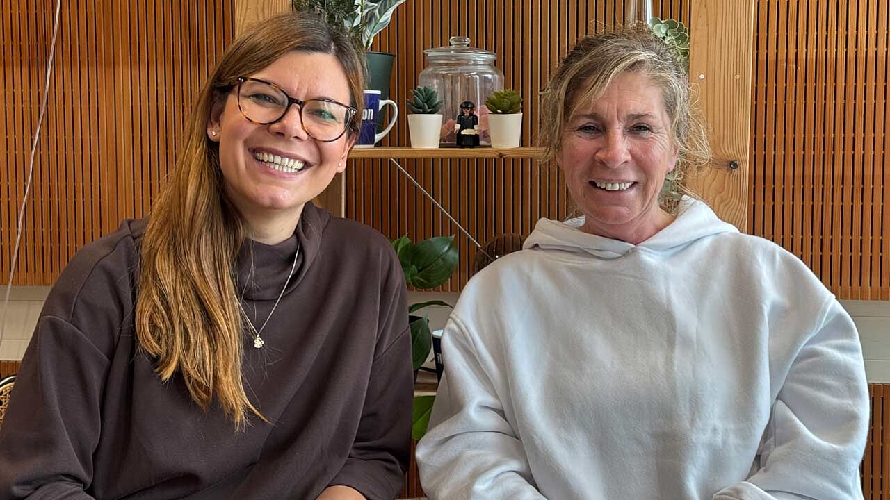 Charlotte Mattes und Christine Sparr lächeln in die Kamera. Sie sitzen im Podcaststudio. 