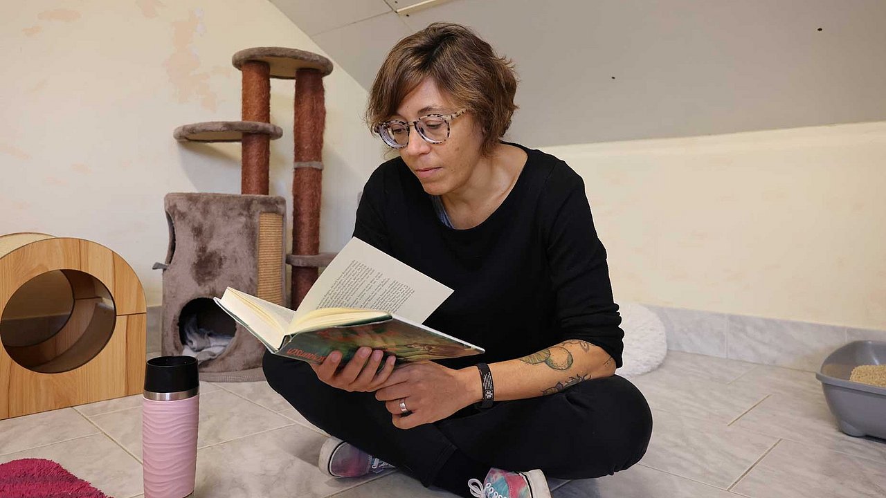 Marlene Dorn liest den scheuen Katzen den "Wunschpunsch" von Michael Ende vor. Sie sitzt im Schneidersitz im Gehege und guckt auf die Buchseiten. 