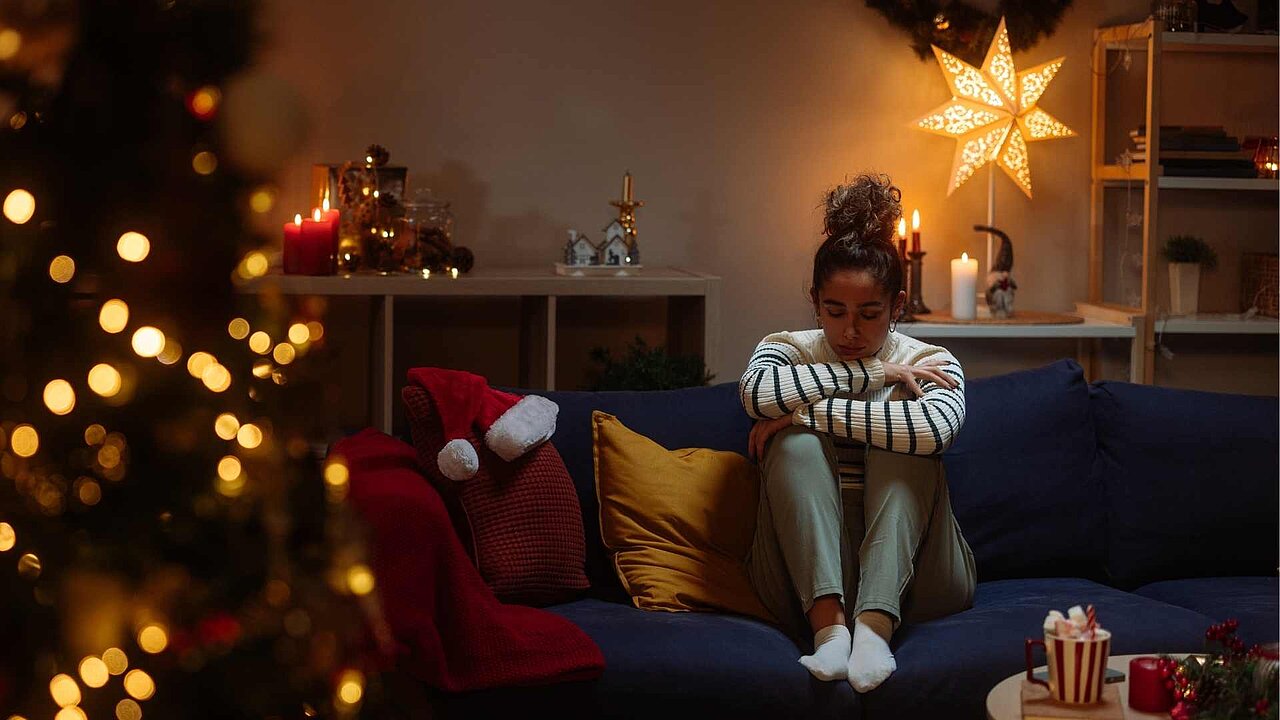 Frau alleine auf dem Sofa inmitten von Weihnachtsschmuck