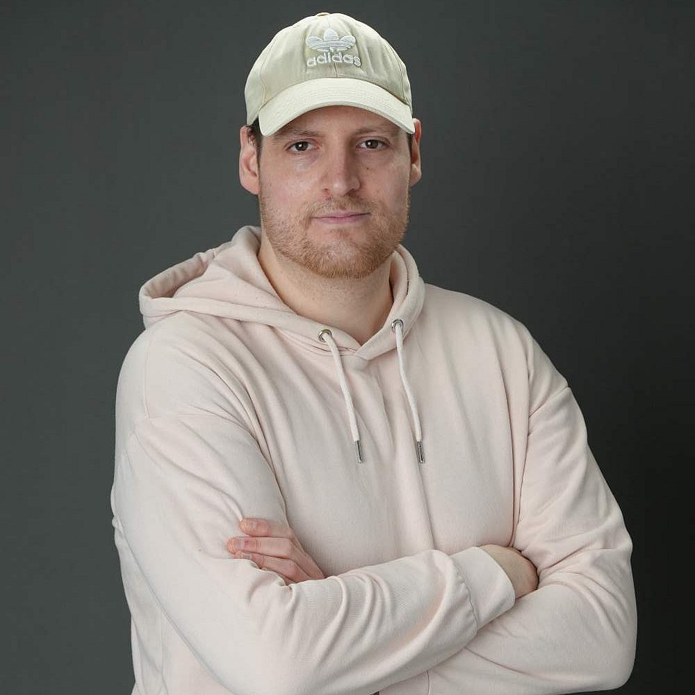 Marco mit pinkem Hoodie und Kappe vor grauem Hintergrund