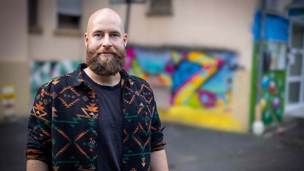 Emil, mit Vollbart und Glatze vor einer Graffiti-Wand