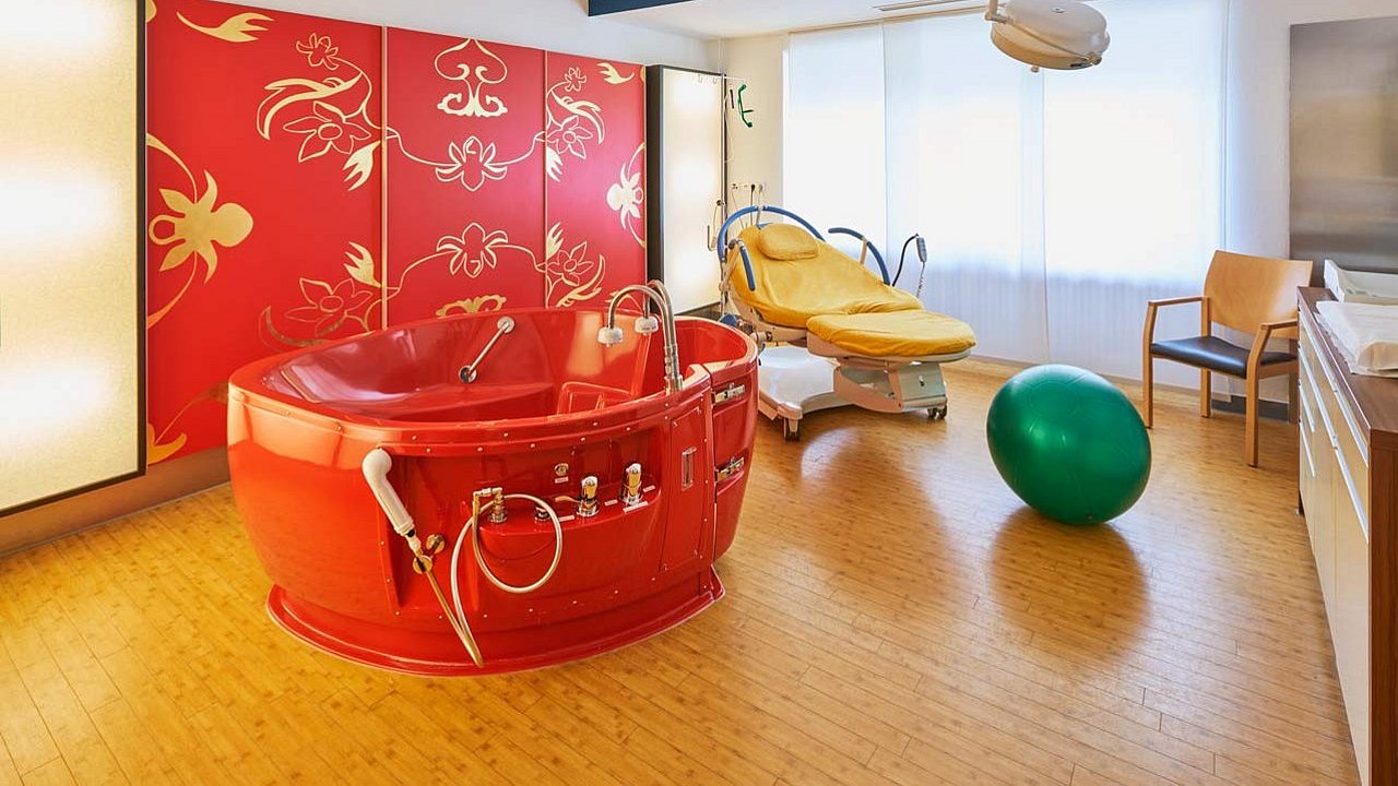 Auf dem Foto ist eine rote Badewanne zu sehen, ein grüner Hüpfball. Alles ist in warmen Licht gehalten. 
