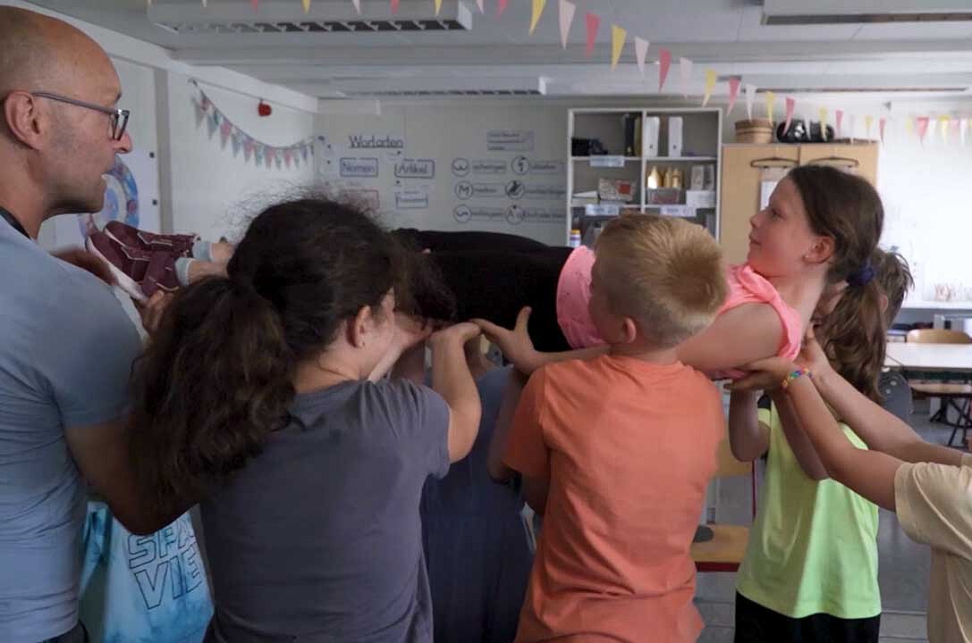 Mehrere Grundschüler:innen heben ein Mädchen hoch