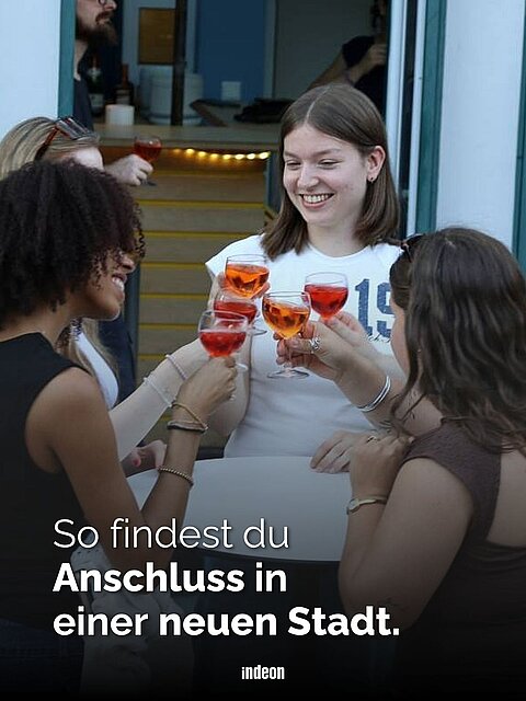 Vier Freundinnen stehen glücklich in einem groß und stoßen mit Getränken an. 