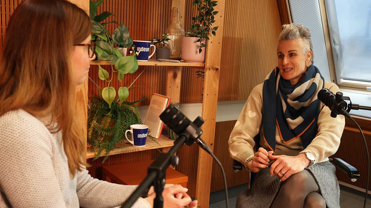 Charlotte Mattes und Sonja sitzen im Podcaststudio und schauen sich an und unterhalten sich. 