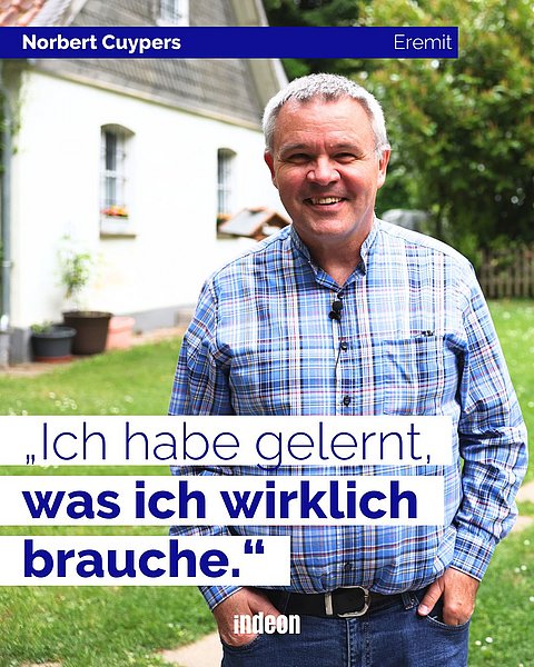 Hemd tragender Mann im Freien, vor einem weißen Haus mit Pflanzen im Hintergrund; Zitat auf Deutsch: „Ich habe gelernt, was ich wirklich brauche.“