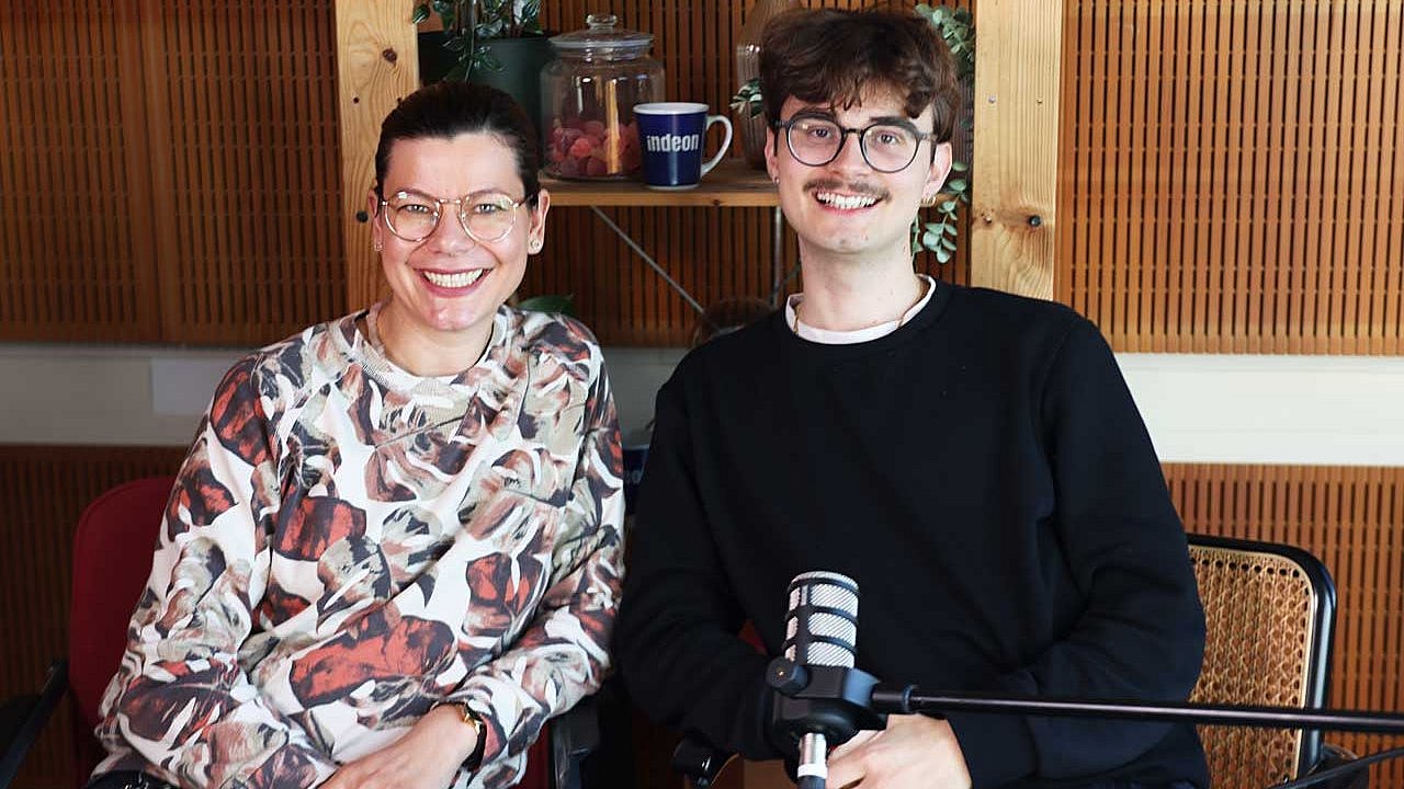 Lotte und Cornelius sitzen im Studio und lachen in die Kamera