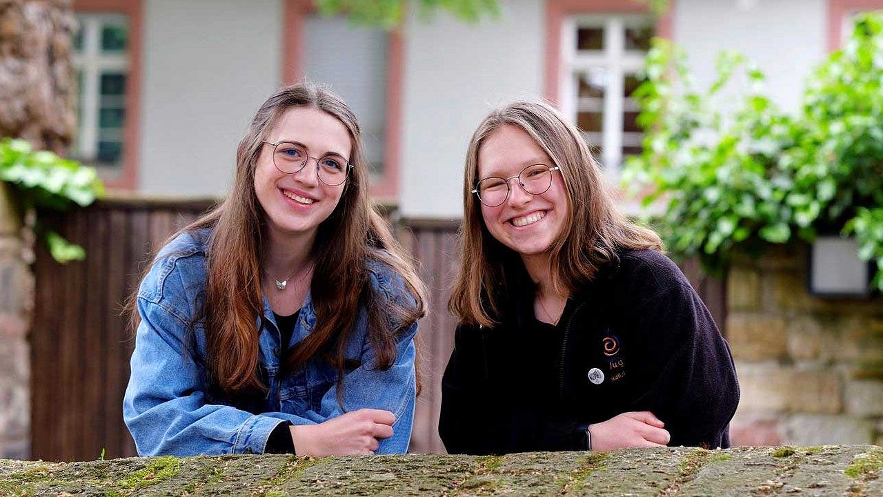 Nina Maskus (rechts) und ihre Freundin Luisa Eizenhöfer stützen sich lächelnd an einer Mauer ab.