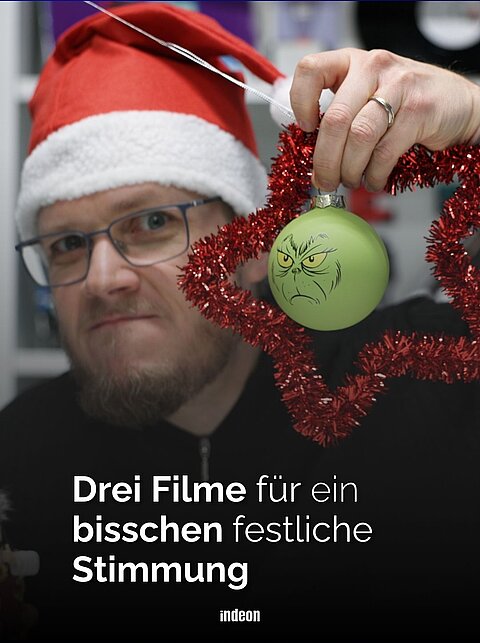 Jörn schaut etwas muffelig in die Kamera und hält eine Grinch Weihnachtskugel hoch
