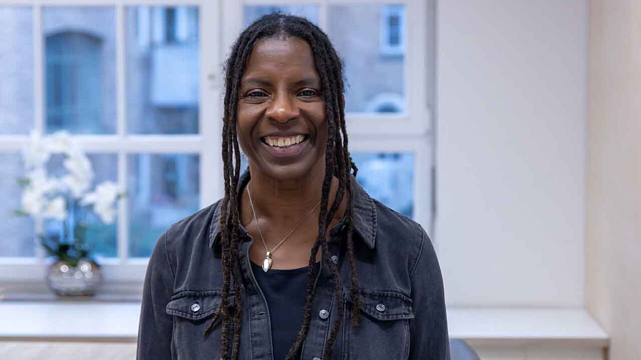 Judy Bailey steht im Medienhaus und lächelt in die Kamera. 