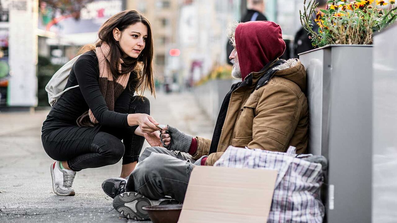 Junge Frau hilft obdachlosem Mann, indem sie ihm Geld gibt. 