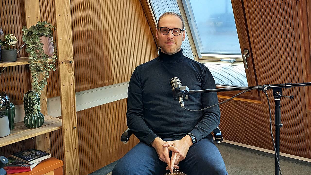 Lukas sitzt auf einem Stuhl im Studio und guckt direkt in die Kamera. 