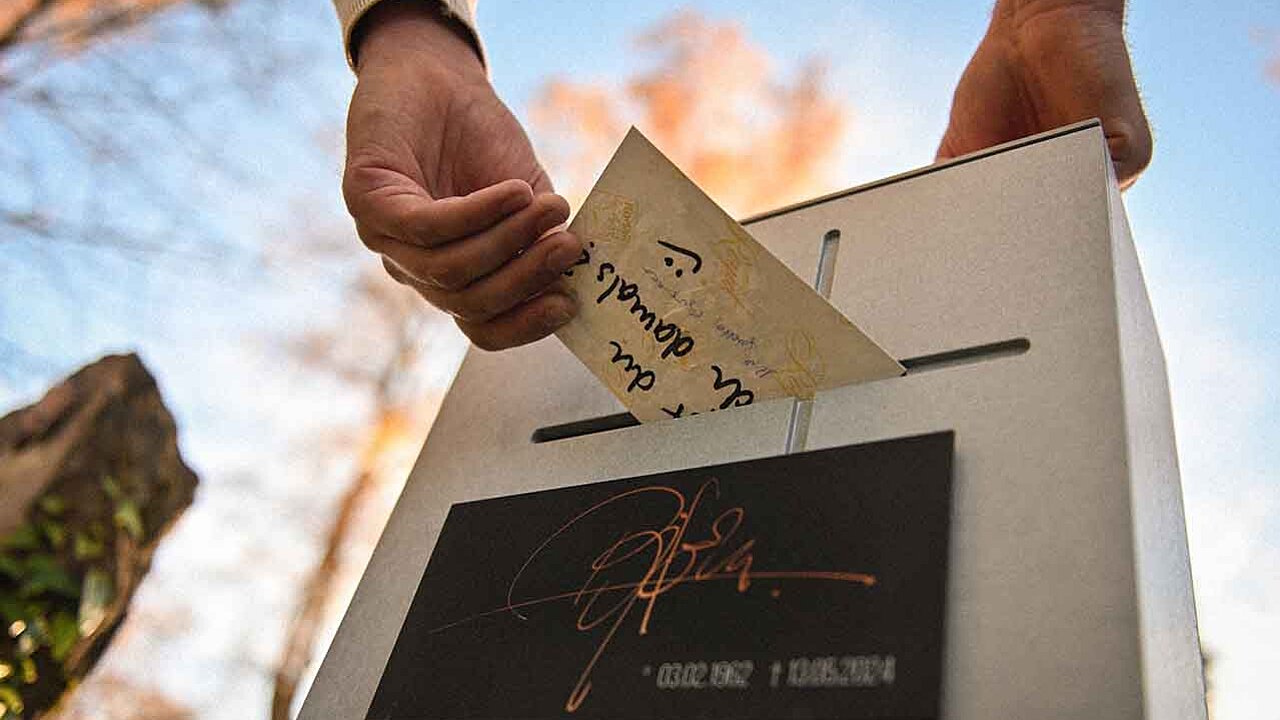 Eine Hand wirft eine Mitteilung in einen Grabstein ein