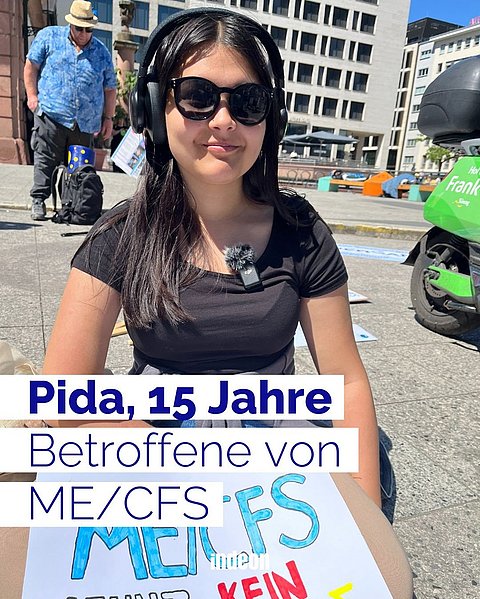 Eine junge Frau mit schwarzen Haaren, Sonnenbrille und schwarzem T-Shirt sitzt auf einem gepflasterten Platz in Frankfurt. Es ist Pida. Sie ist 15 Jahre alt und hat ME/CFS.