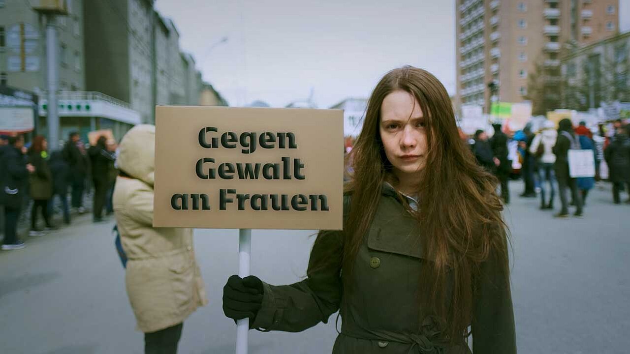 Junge Aktivistin bei einer Demonstration. Auf ihrem Schuld steht: Gegen Gewalt an Frauen.