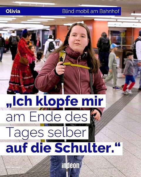 Eine junge Frau mit braunen Haaren, einer rotbraunen Jacke und mit Blindenstock steht im Bahnhof. Das ist Olivia. Im Hintergrund sind zahlreiche Menschen. Text: Olivia. Mobil am Bahnhof. „Ich klopfe mir am Ende des Tages selber auf die Schulter.“
