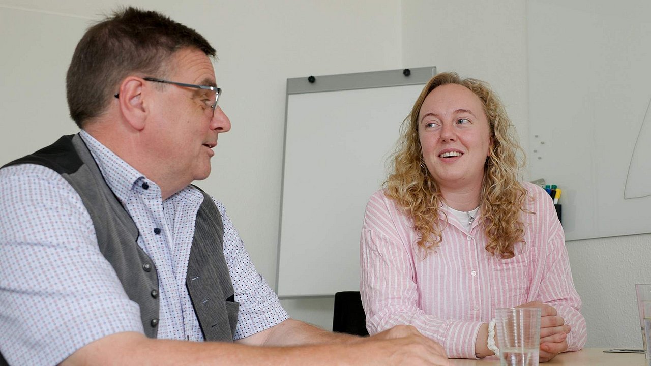 Sozialarbeiterin Nina Wöllert strahlt, während sie etwas erzählt. Stefan Buckendahl hört ihr aufmerksam zu. Beide sitzen an einem Tisch