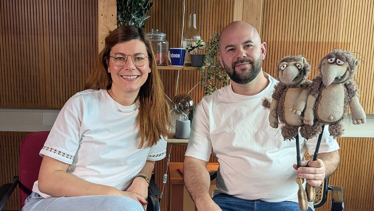 Charlotte Mattes (Host) und Ricardo Sperlich im Studio. Ricardo hält zwei Puppen hoch. Urzeitratten, die er im Stück Furzipups spielt. 