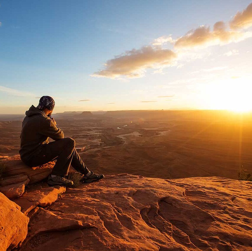 Ein Wanderer blickt in den Sonnenuntergang am großen Aussichtspunkt im Canyonlands National Park in Utah, USA.