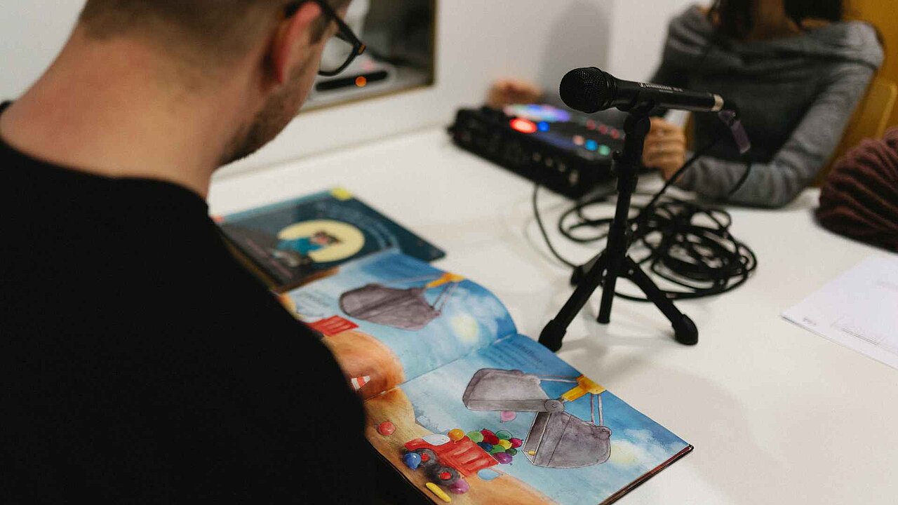 Ein Häftling liest aus einem Kinderbuch vor. Studentinnen zeichnen das auf.