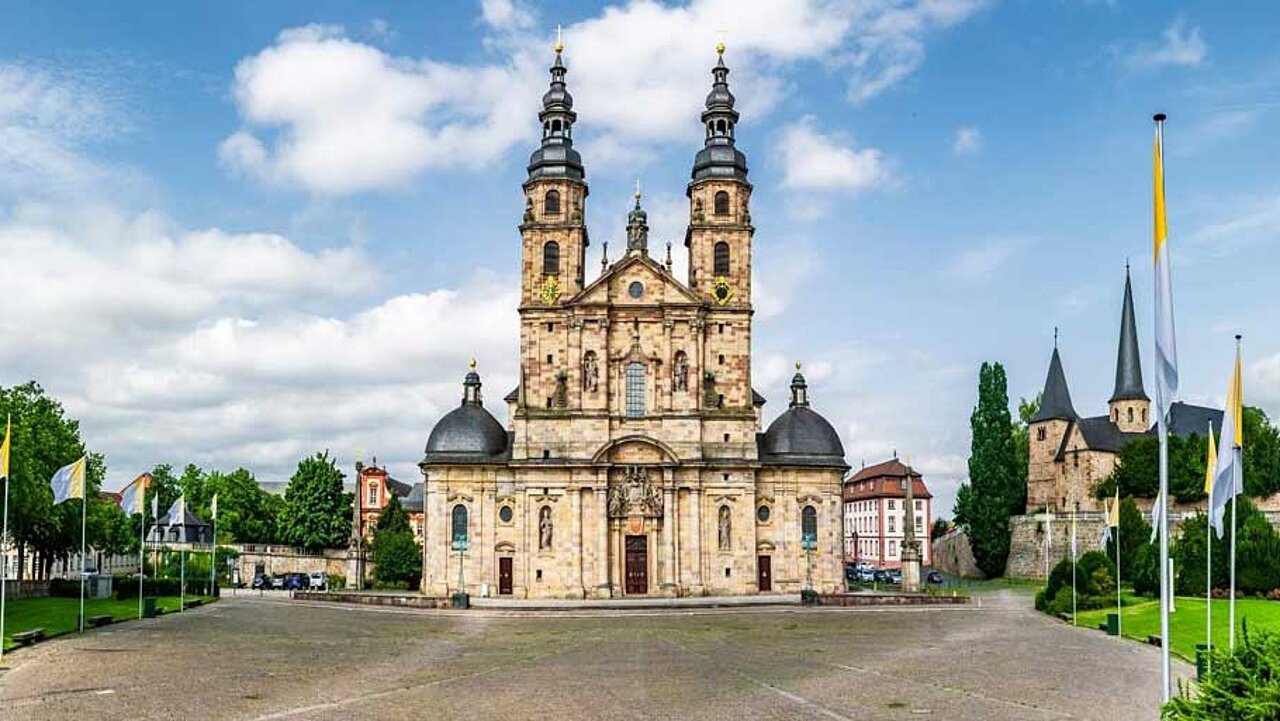 Das historische Domgebäude mit Domvorplatz. Rundherum Bäume und Fahnenmasten.