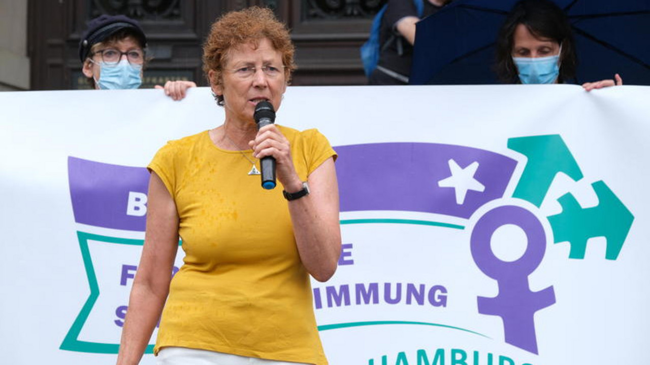 Ältere Frau mit gelbem Shirt und weißer Hose hält ein Mikro