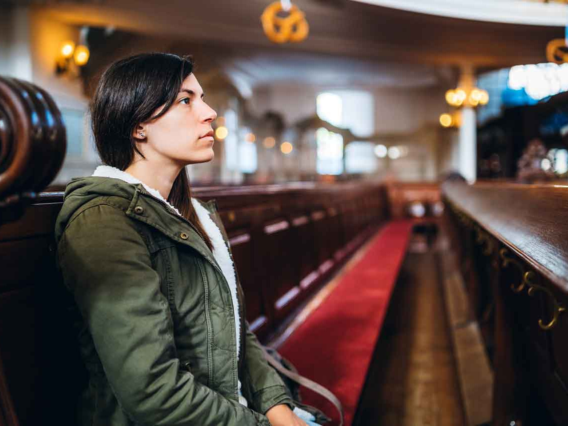 Frau sitzt alleine in einer Kirchenbank