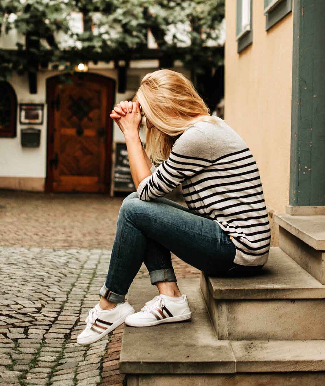Daniela sitzt auf einer Treppe und stützt den Kopf zweifelnd in ihre Hände. Im Hintergrund ein Fachwerk-Haus.