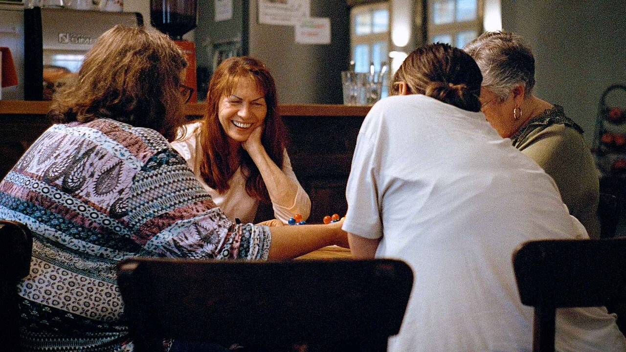 4 Frauen sitzen an einem Tisch. Sie unterhalten sich, spielen und trinken Kaffee.