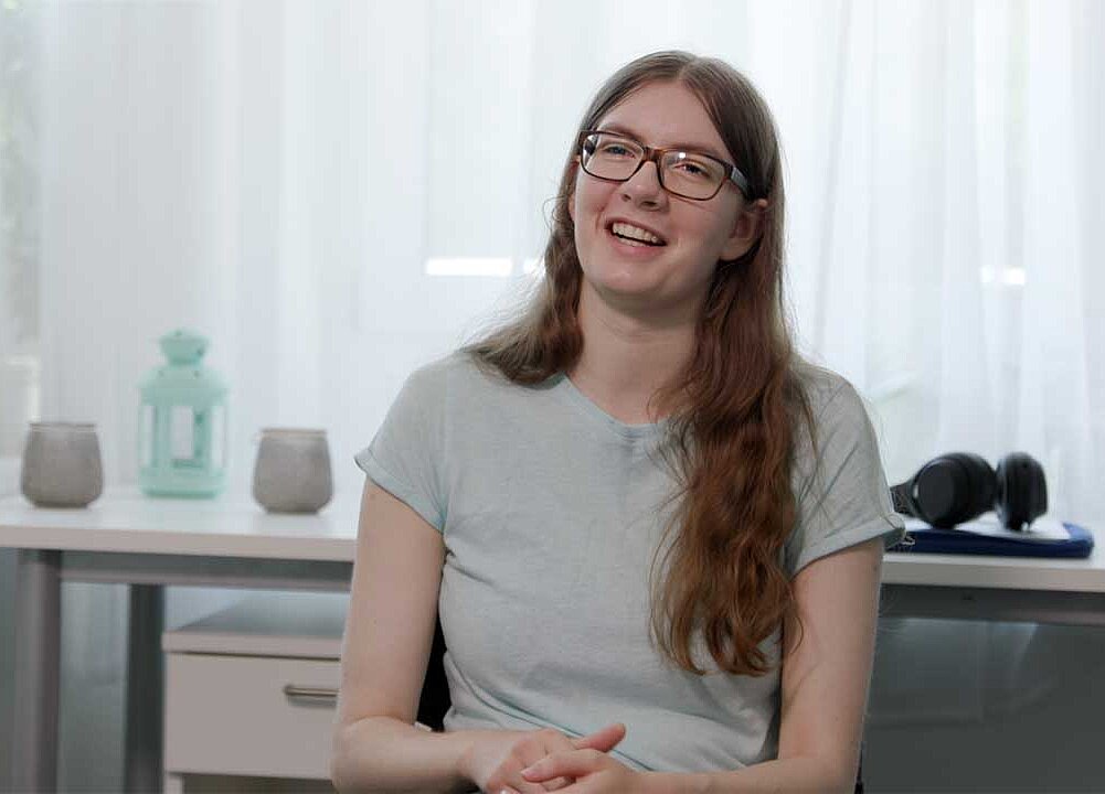 Jana sitzt vor einem Fenster und erzählt. 