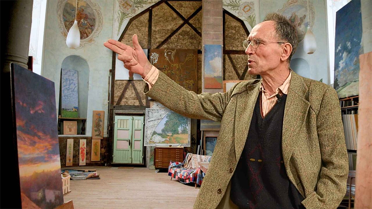 Collage: Im Hintergrund das Atelier von Forster mit seinen Bildern aka der Altarraum, im Vordergrund steht er und zeigt in den Raum hinein