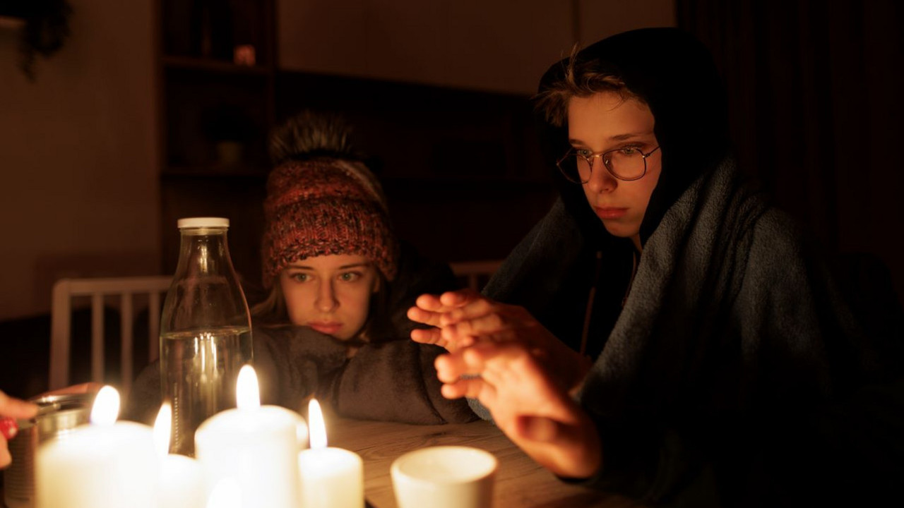 Zwei Kinder wärmen sich die Hände an brennenden Kerzen.