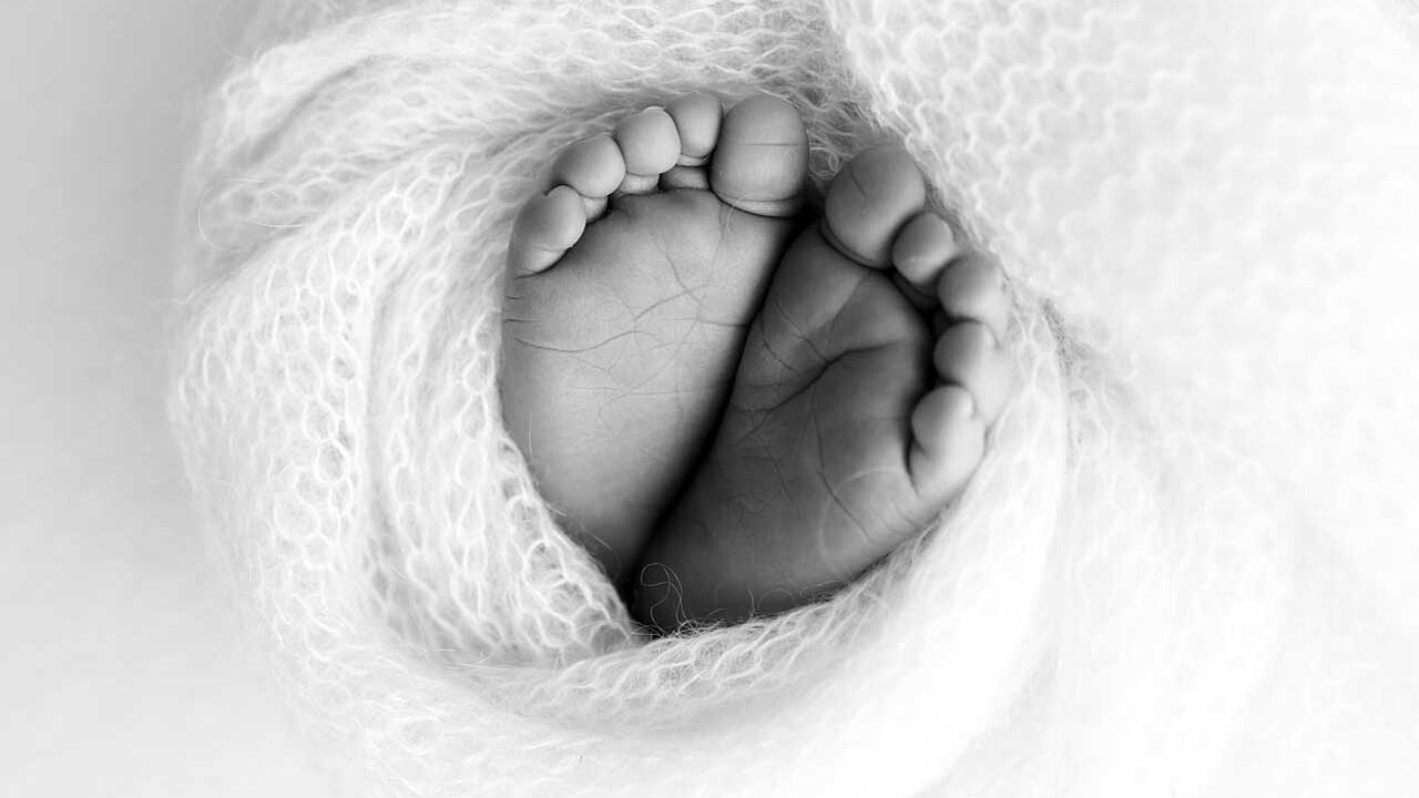 kleine Babyfüße umhüllt von einer weichen, weißen Decke. Die Aufnahme ist schwarz-weiß.