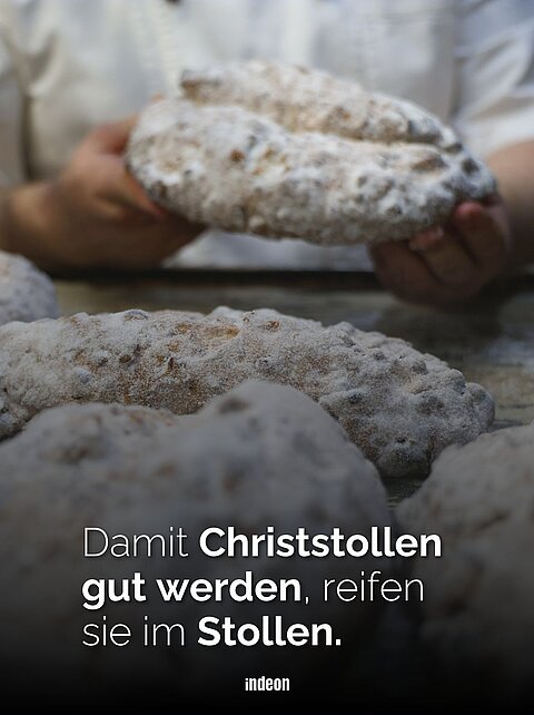 Im Vordergrund liegen fische Christstollen auf einem Backblech. Dahinter halten die Hände eines Bäckers einen weiteren Stollen. 