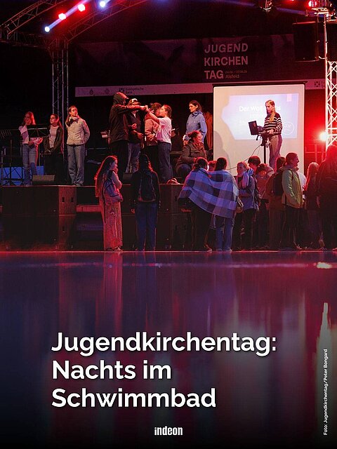 Eine Bühne in der Nacht. Beleuchtet mit roten Lichtern, vor der glatten Wasseroberfläche eines Schwimmbeckens. Darin Spiegelungen. Text: Jugendkirchentag: Nachts im Schwimmbad.