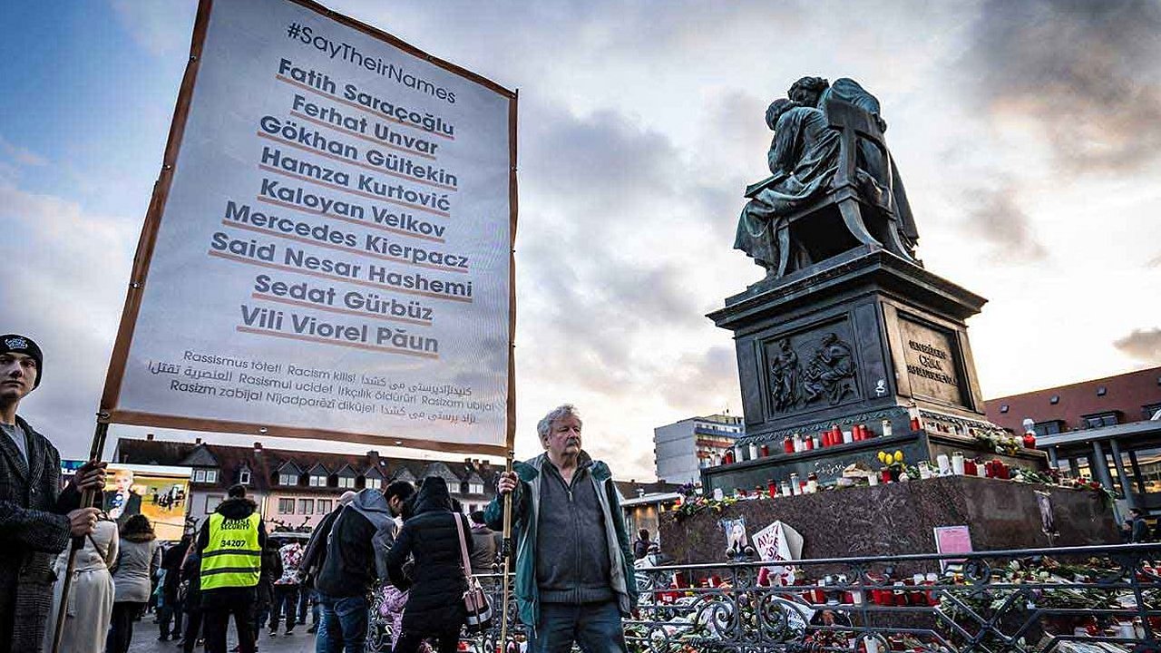 Plakat mit den Namen der Opfer aus Hanau, Blumen, Kränze und Kerzen am Brüder-Grimm-Denkmal auf dem Marktplatz 