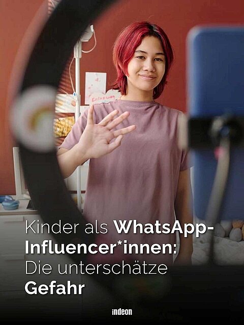 Man blickt beim Betrachten des Bildes von hinten durch ein Ringlicht. Zu sehen ist eine Jugendliche. Sie trägt kurze rote Haare, lacht und winkt in Richtung Kamera. 