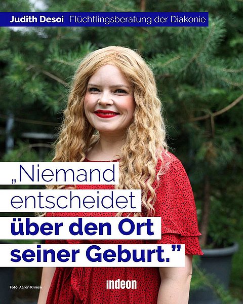 Eine weiße Frau mit langen blonden Haaren, rotem Lippenstift und rotem Oberteil vor einem Baum. Sie lächelt. Das ist Judith. Text: "Judith Desoi: Flüchtlingsberatung der Diakonie. Niemand entscheidet über den Ort seiner Geburt."